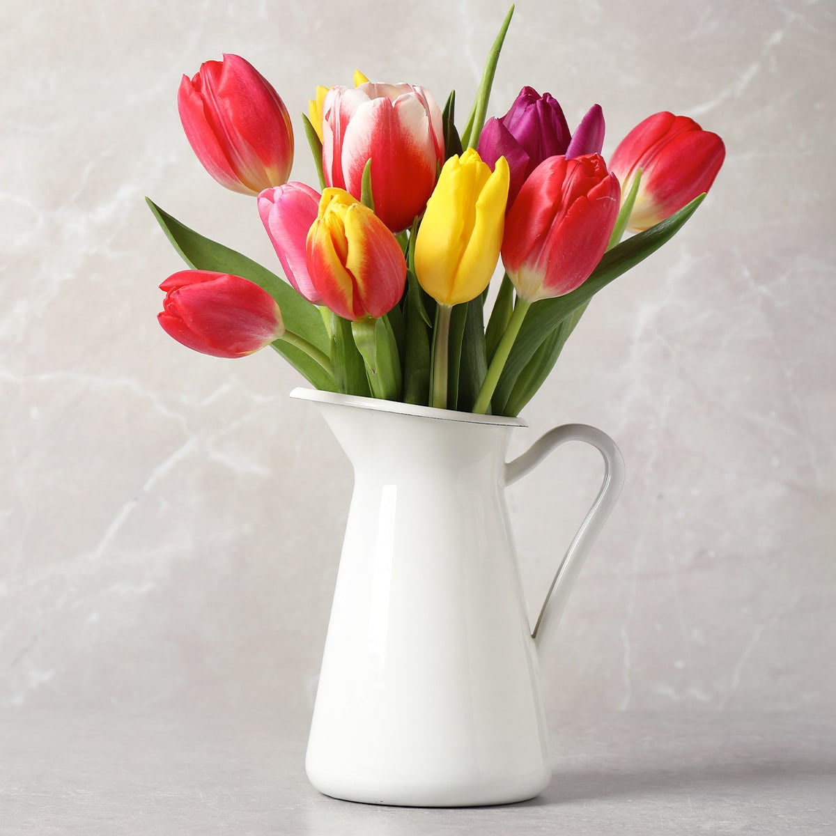 A mix of red, yellow and purple tulips inside a white pitcher